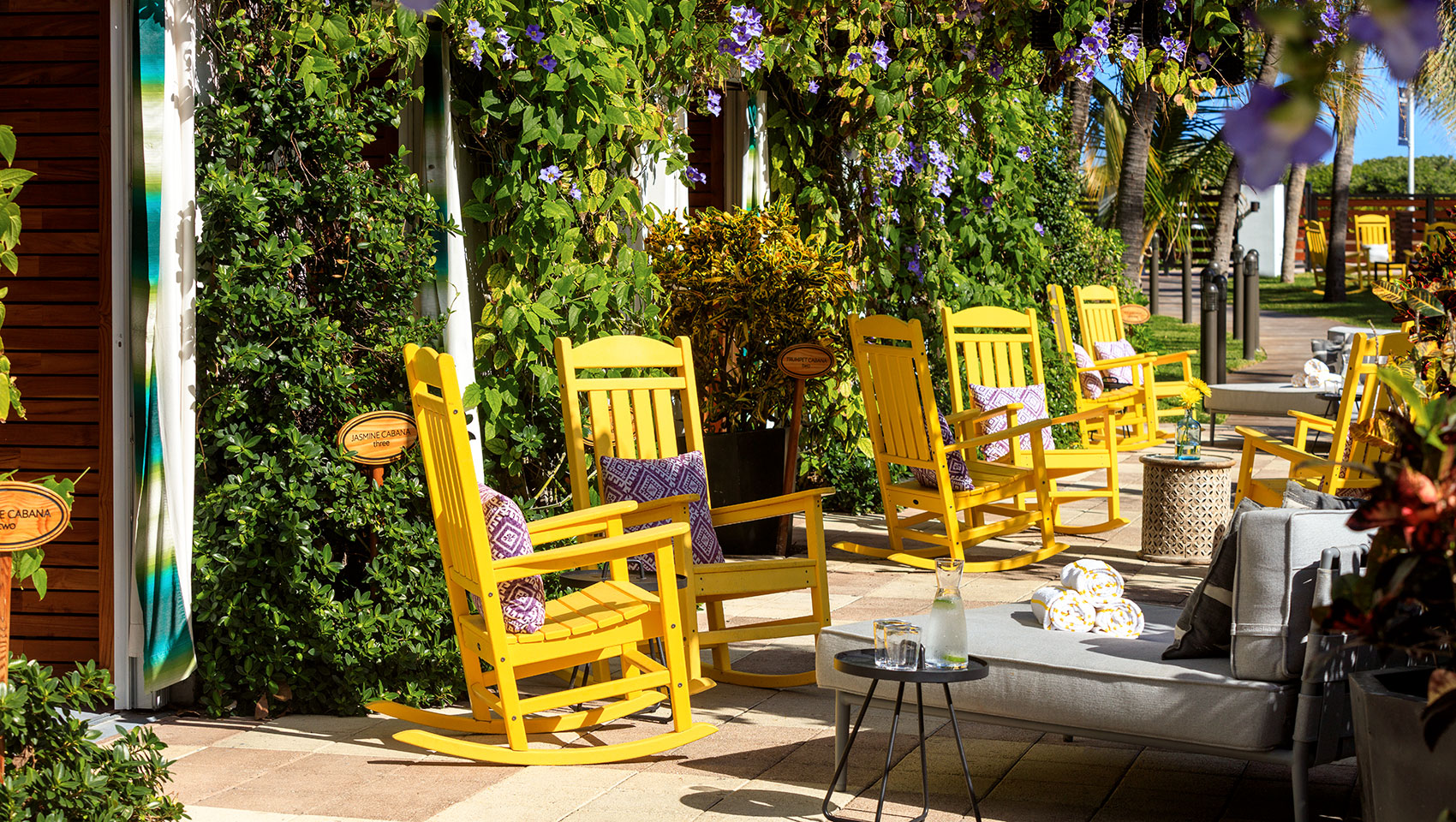 walkway next to pool with cabanas and rocking chairs for lounging