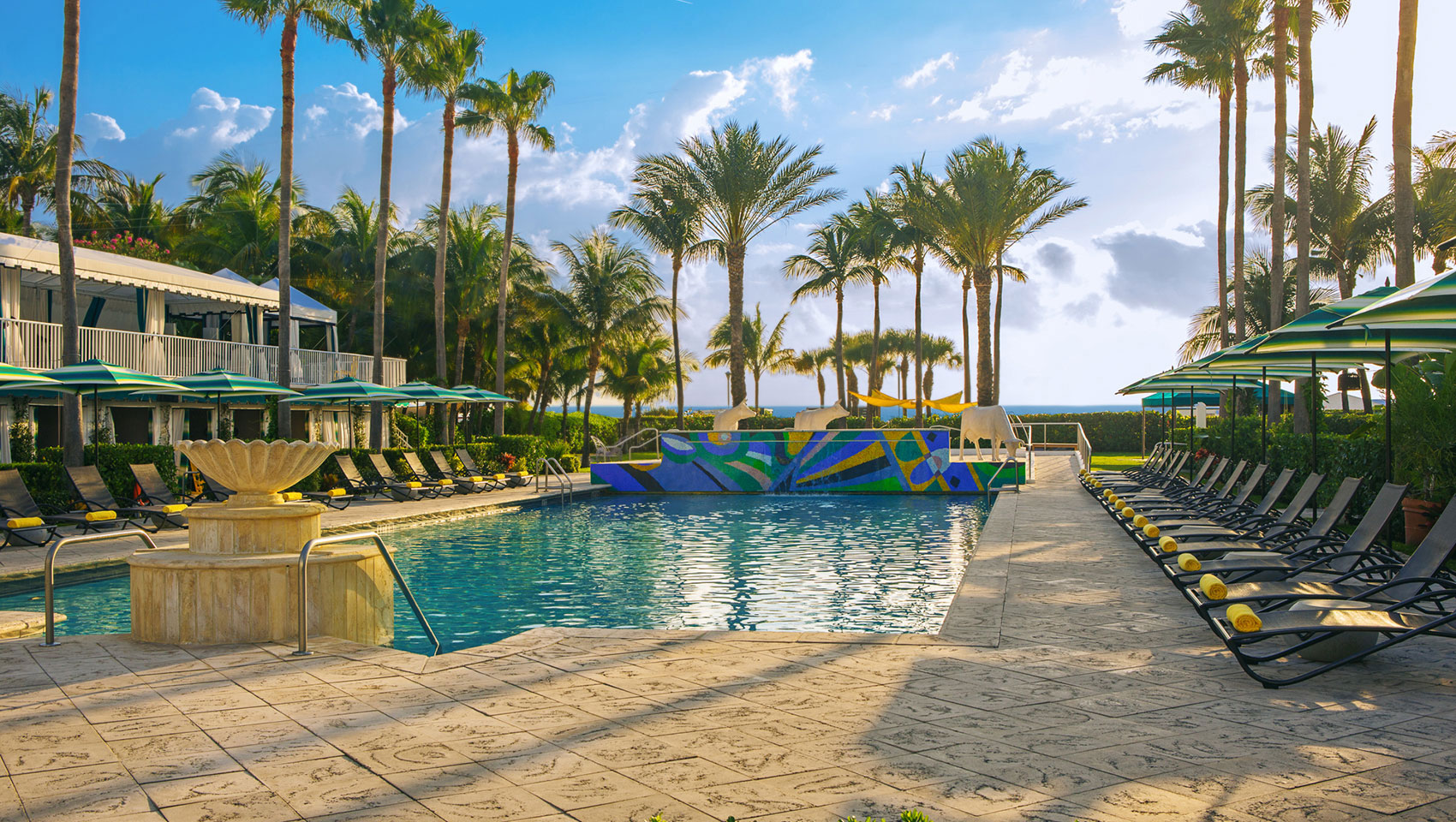 pool and lounge chairs with palm trees and clounds in the sky